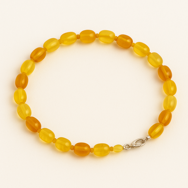 Collier en perles ovales d'ambre jaune et miel, disposé en cercle sur fond blanc lumineux.